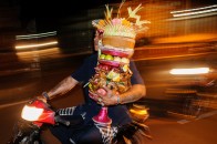 Seorang pria mengendarai sepeda motor dengan membawa sesajen beralaskan dulang seusai dihaturkan saat upacara di Pura Dalem Desa Abianbase, Gianyar.